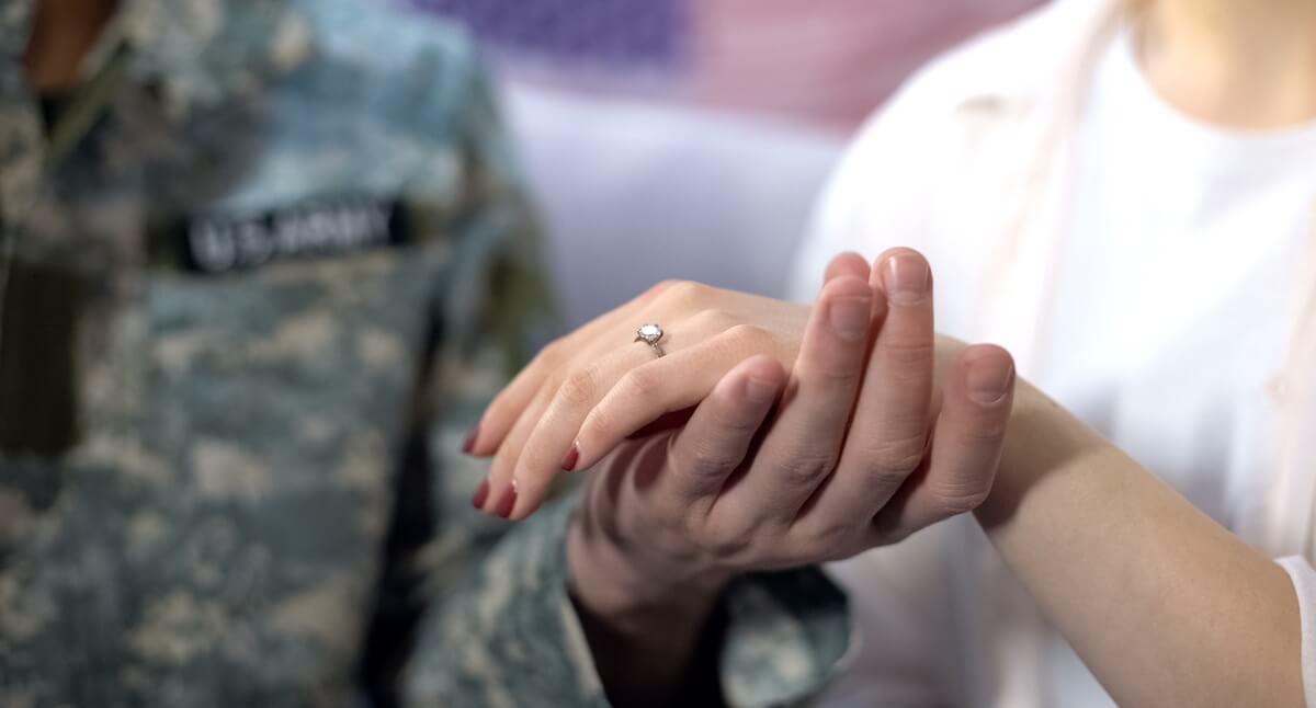 US service member holds ringed hand of his foreign national spouse