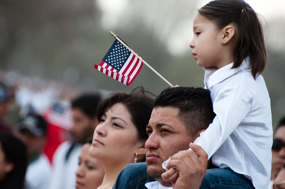 Child holding American flag sits on father's shoulders